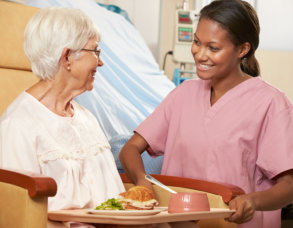 Nurse Serving Meal To Senior Female Patient Sitting In Chair